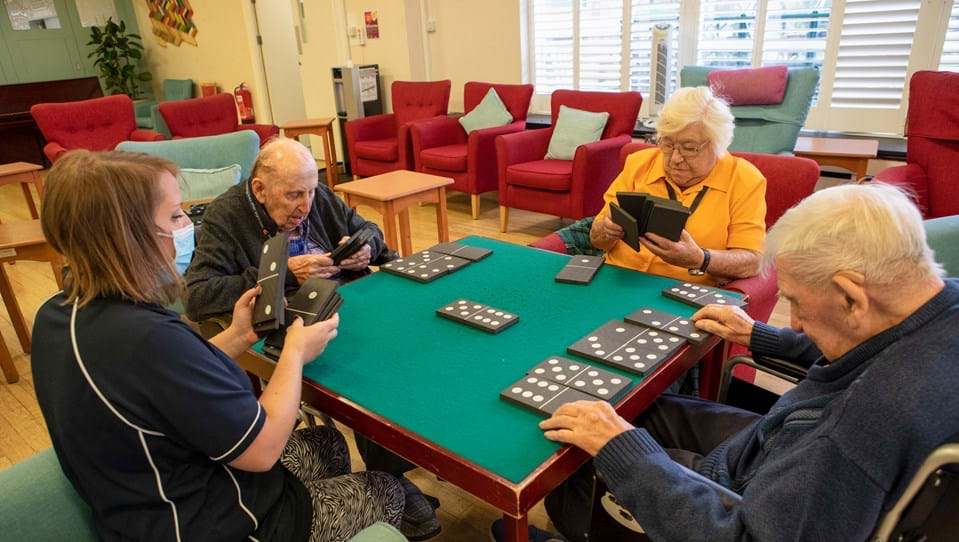 Blind veterans sitting at a table with a Blind Veterans UK activities facilitator playing a game of dominos with large pieces