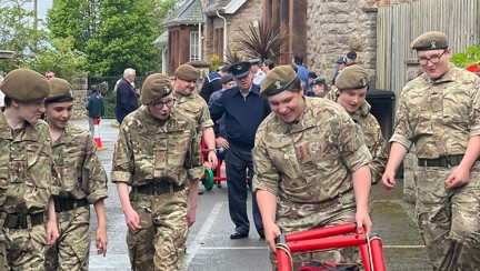 Army cadets smiling and laughing while looking at something they have built made of red plastic poles