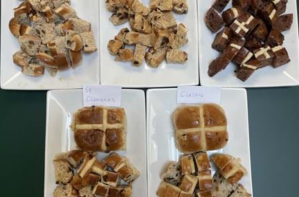 5 oblong white plates are set out on a green table each with one whole hot cross bun and a pile of hot cross bun pieces