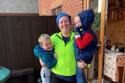 Charity supporter Sam, wearing running gear and holding up her two sons in her arms