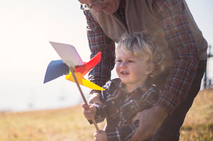 A grandad leaning over his grandson as he plays with a windmill toy