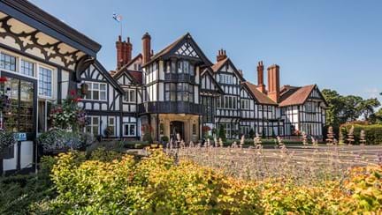 The front entrance of Petwood Hotel, a Tudor-style building, surrounded by lush garden and flowering plants.