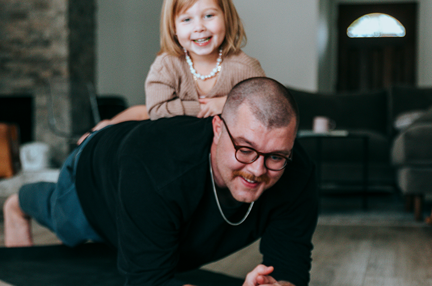 A photo of a supporter planking and laughing with his young daughter leaning on him