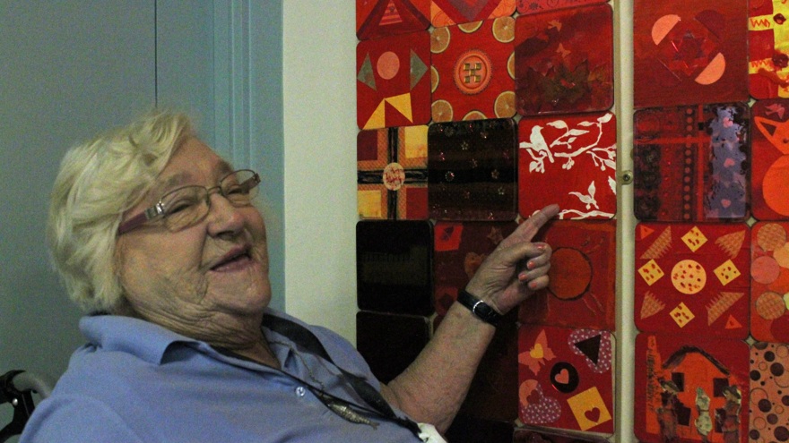 Blind veteran, Win, smiling and pointing to her tile in the Collaboration in Colour artwork