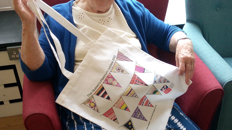 Blind veteran Betty pictured sitting down on a chair holding up her jubilee bunting bag