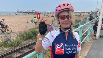 Rider Emilia in her Blind Veterans UK cycling top holding her medal up proudly.  The beach and Brighton Pier can be seen in the background.