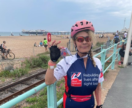 Rider Emilia in her Blind Veterans UK cycling top holding her medal up proudly. The beach and Brighton Pier can be seen in the background.