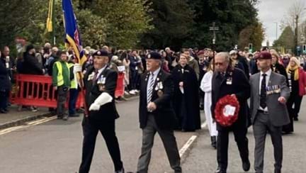 Alan holding the Blind Veterans UK Standard and walking beside blind veteran Jim