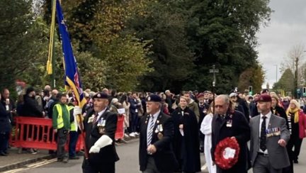 Alan holding the Blind Veterans UK Standard and walking beside blind veteran Jim