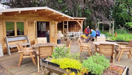 A wood cabin, with a wooden patio and seating area with plants