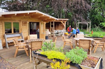 A wood cabin, with a wooden patio and seating area with plants