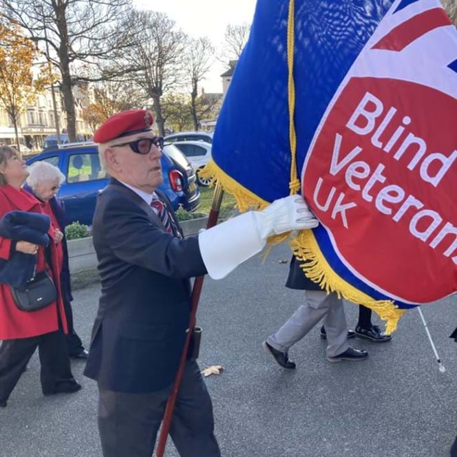 John wearing his medals holding the Blind Veterans UK flag