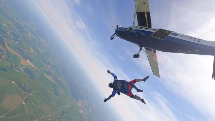 Mark and the tandem instructor falling headfirst in freefall before the parachute is opened. The plane is above them and the fields below