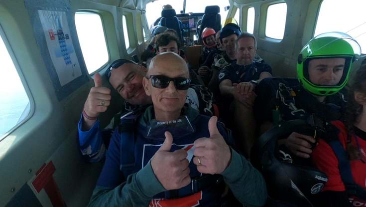 Mark with two thumbs up onboard the plane with a group of other jumpers and instructors