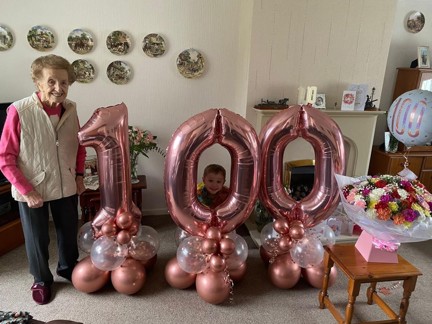 Blind veteran Margaret stands beside huge pink balloons that read '100'