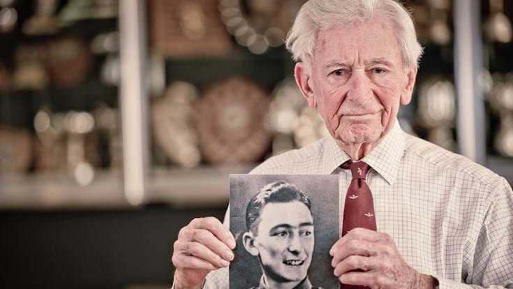 Blind veteran Jim holding a black and white photograph of himself during his days in service