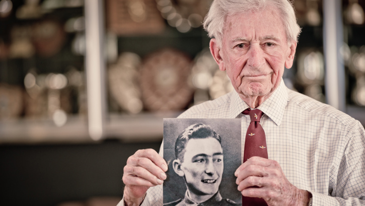 Blind veteran Jim holding a black and white photograph of himself during his days in service