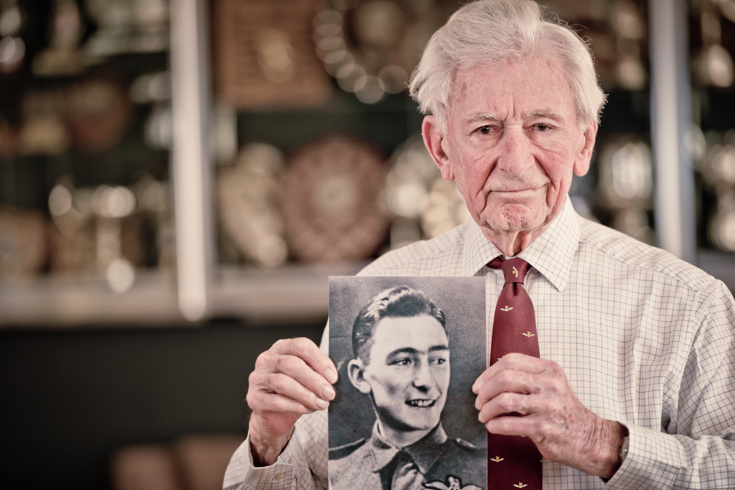 Blind veteran Jim holding a black and white photograph of himself during his days in service