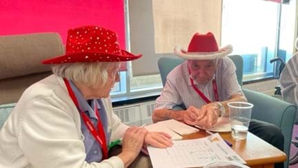 Blind veteran Jack with partner Ellen both wearing red hats while eating Christmas cake