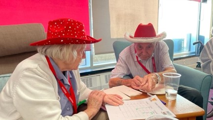 Blind veteran Jack with partner Ellen both wearing red hats while eating Christmas cake