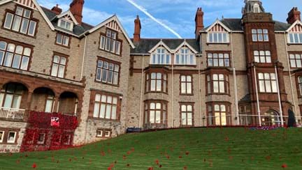 The outside of the Llandudno Centre of Wellbeing photographed with a curtain of poppies displayed from a balcony and poppies spreading out over the lawn
