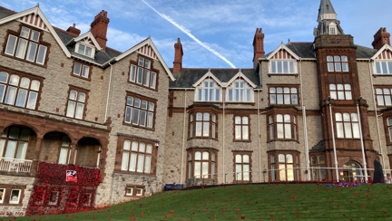 The outside of the Llandudno Centre of Wellbeing photographed with a curtain of poppies displayed from a balcony and poppies spreading out over the lawn