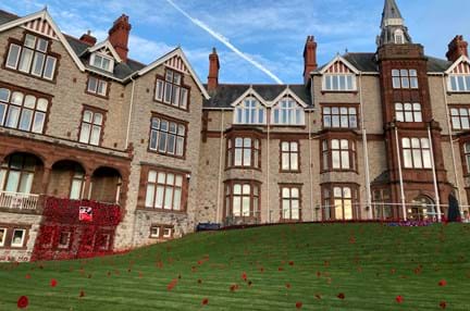 The outside of the Llandudno Centre of Wellbeing photographed with a curtain of poppies displayed from a balcony and poppies spreading out over the lawn