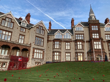 The outside of the Llandudno Centre of Wellbeing photographed with a curtain of poppies displayed from a balcony and poppies spreading out over the lawn