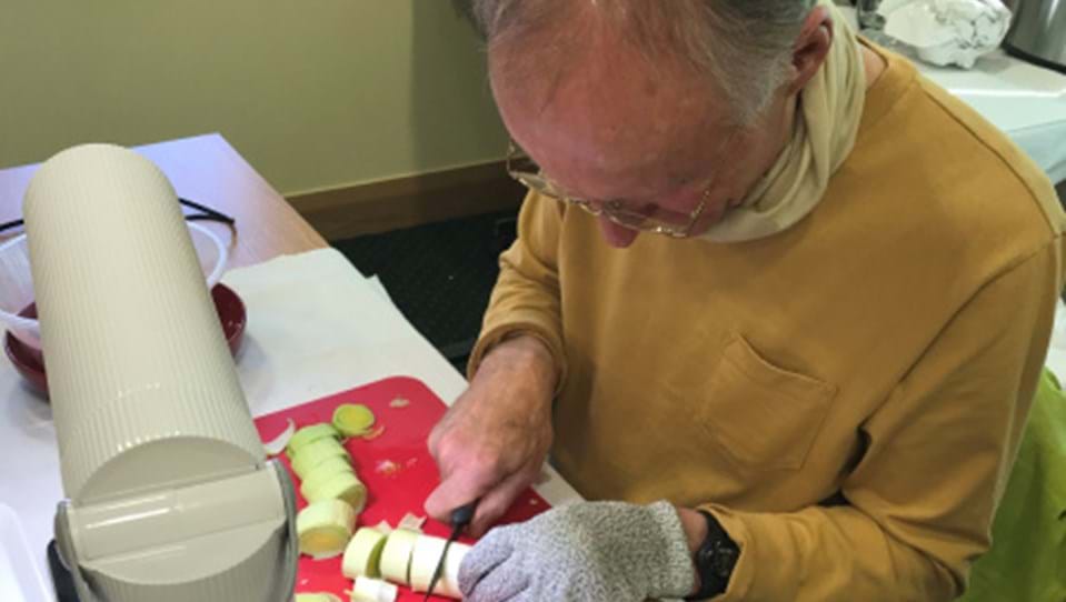 Blind veteran cutting vegetables on a chopping board under a bright desk lamp