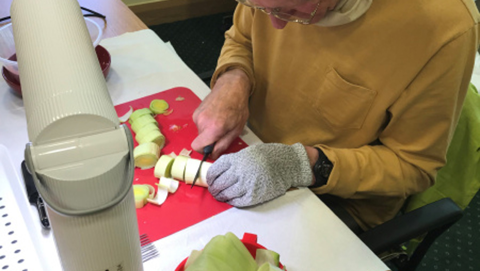 Blind veteran cutting vegetables on a chopping board under a bright desk lamp