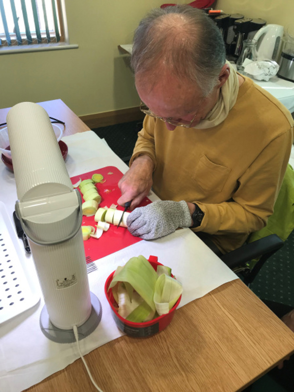 Blind veteran cutting vegetables on a chopping board under a bright desk lamp