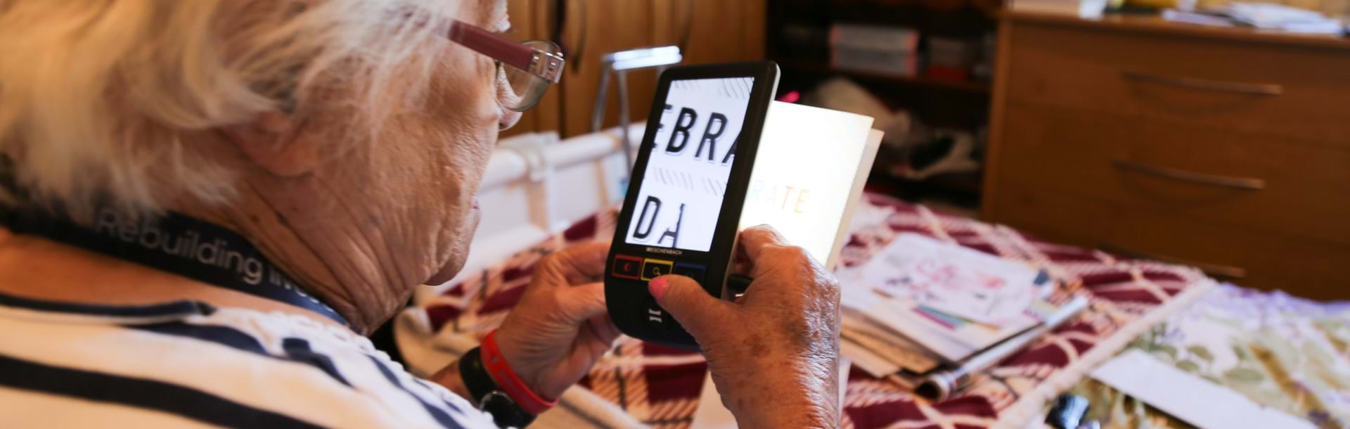 Blind veteran Win using a handheld electronic magnifier to read text on a card