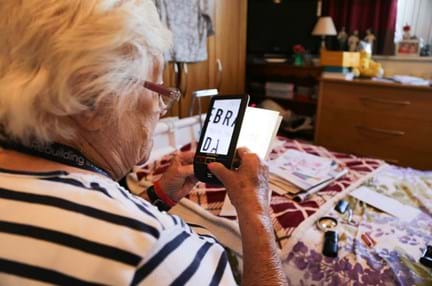 Blind veteran Win using a handheld electronic magnifier to read text on a card