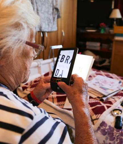 A photo of blind veteran Win using a handheld electronic magnifier to read a card