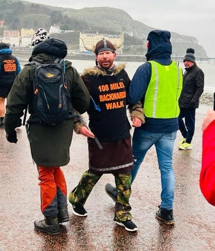 Supporter walking backwards dressed as a Viking and being supported by two forward facing walkers holding each arm