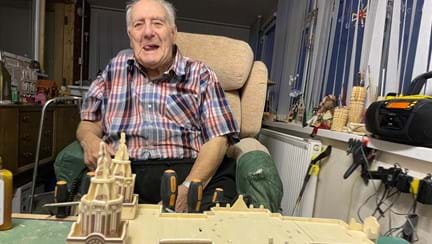 Maurice is smiling and sitting in front of a large model of a cathedral