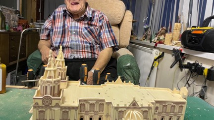 Maurice is smiling and sitting in front of a large model of a cathedral