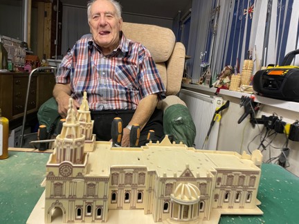 Maurice is smiling and sitting in front of a large model of a cathedral