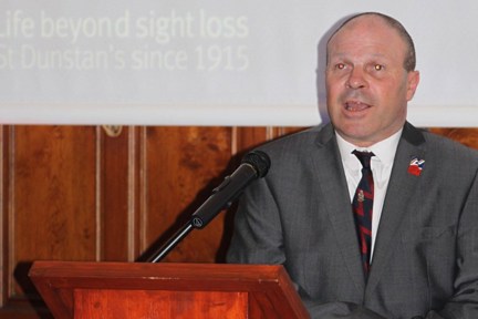 Blind veteran Billy at a podium making a speech at Founders Day event