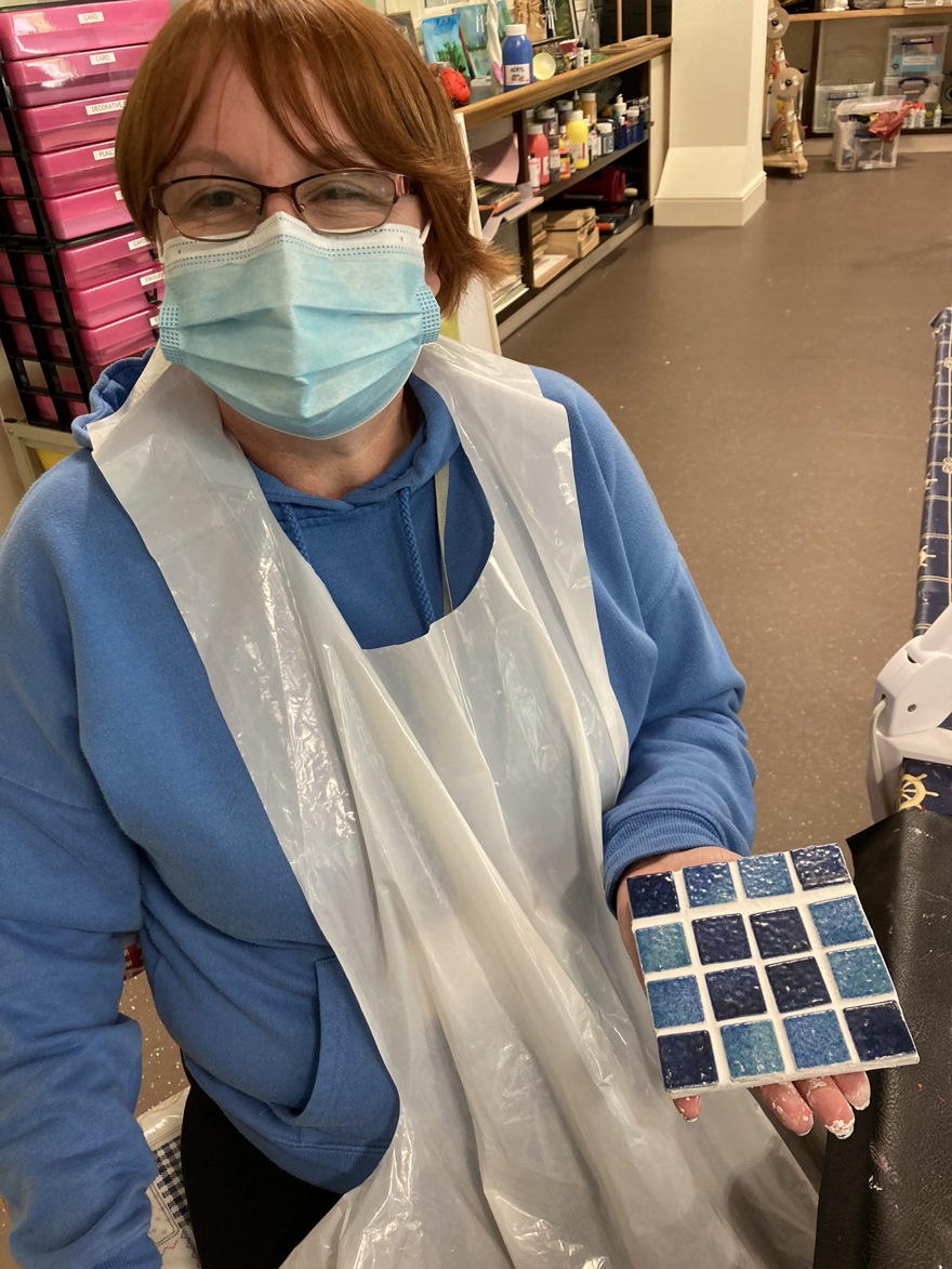 Blind veteran Sheila holding a square mosaic piece in tiles of different shades of blue