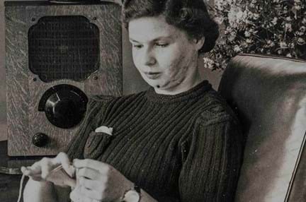An archive photograph of a young blind veteran Barbara sitting on an armchair and sewing