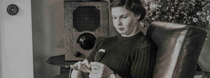 An archive photograph of a young blind veteran Barbara sitting on an armchair and sewing