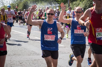 Photo of blind veteran Alan Lock, right and guide Dan, left, running past wearing Blind Veterans UK vest and waving at the camera