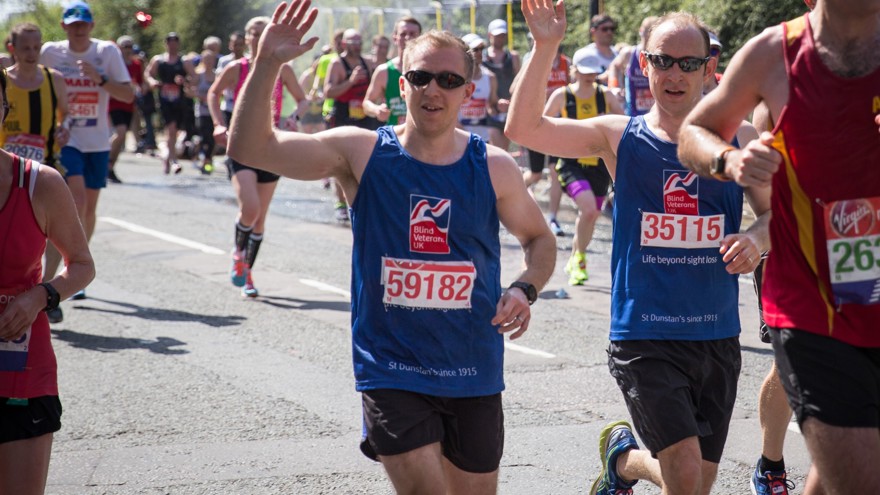 Photo of blind veteran Alan Lock, right and guide Dan, left, running past wearing Blind Veterans UK vest and waving at the camera