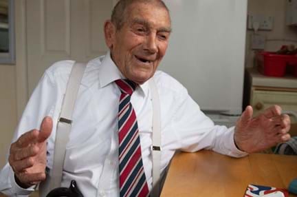 Blind veteran Eddie sitting in his kitchen, laughing while talking to his support worker