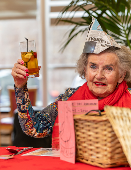 A blind veteran wearing a party hat, holding up a beverage and smiling