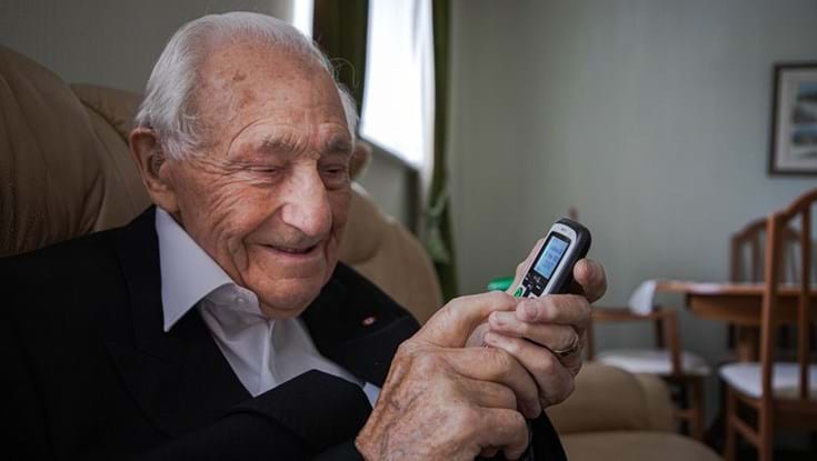 Blind veteran Ron in his living room, smiling as he holds a phone
