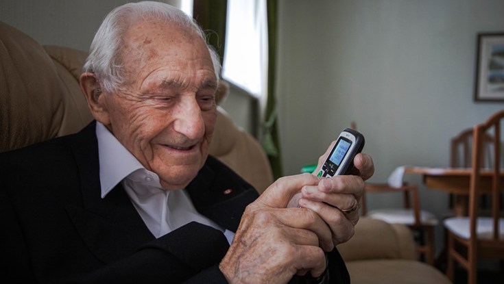 Blind veteran Ron in his living room, smiling as he holds a phone