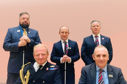 photo of the signing of the Armed Forces Covenant. Commodore Bellfield On Behalf Of The Mod And Nick Caplin On Behalf Of Blind Veterans UK sitting. With three blind veterans standing behind..