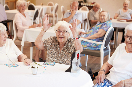 A photo of a group of elderly woman playing bingo with one cheering as she won